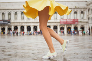 A woman wearing a yellow skirt and yellow shoes dances outside. Her legs are bare.